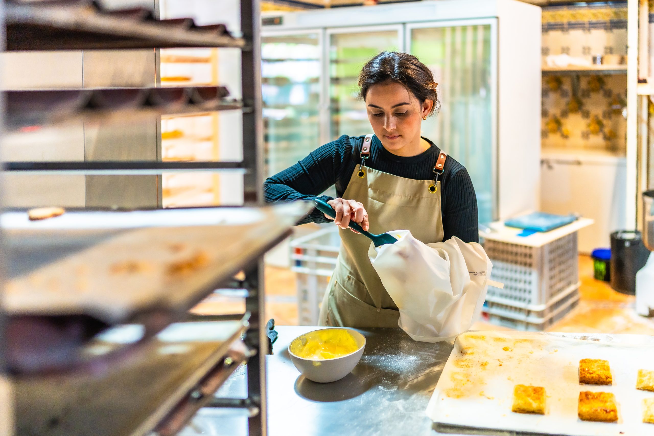 Female latin artisan baker filling a piping bag to decorate pastries in the workshop kitchen of a bakery in Denver, Colorado
